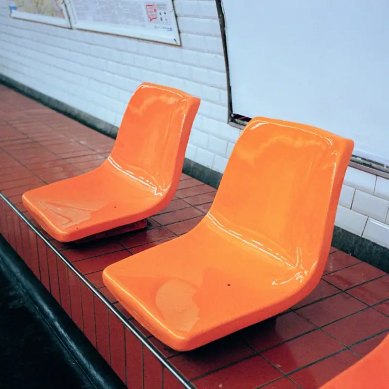 Three orange seats on a Paris metro platform against a tiled wall.